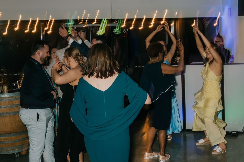 People dancing together at a dimly lit party or nightclub venue with colorful lights in the background.
