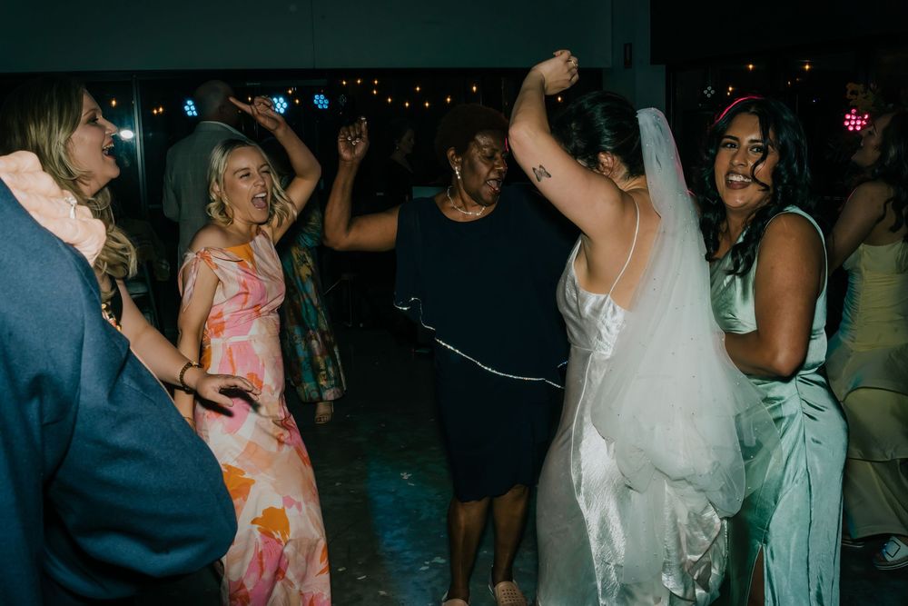 People dancing and celebrating at a festive party with dimmed lighting and decorative elements in the background.