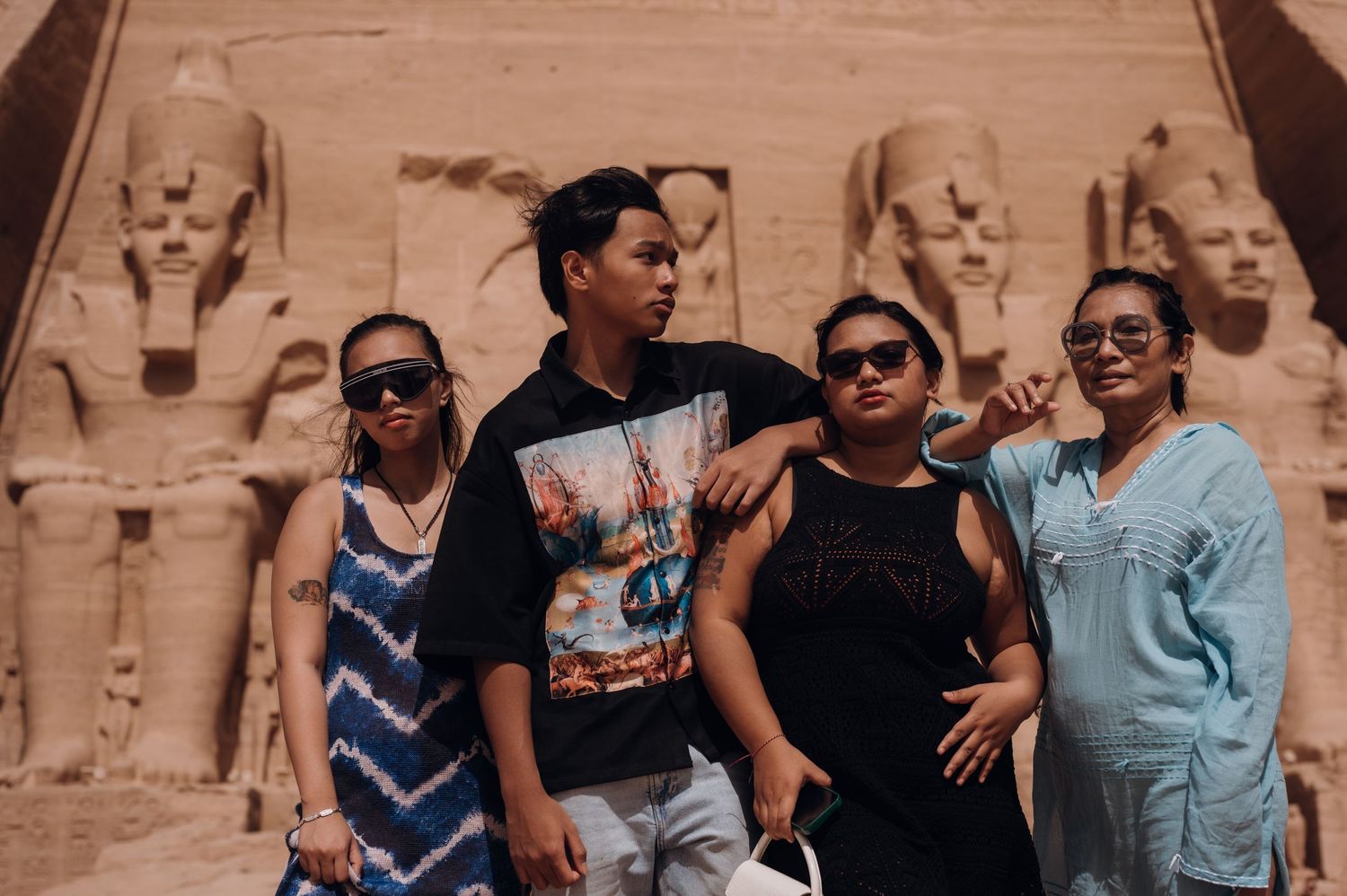 A group poses together in front of ancient Egyptian statues and ruins at Abu Simbel temple.