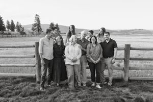 Group photo of people sitting on a wooden fence with a scenic mountain landscape behind them.