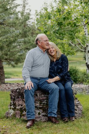 Happy older couple sitting on a stone bench outdoors, sharing a joyful moment surrounded by lush green trees.