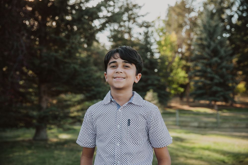 A young person in a collared shirt smiles outdoors on a sunny day.