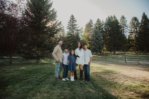A family group poses together on grassy terrain with evergreen trees in the background.