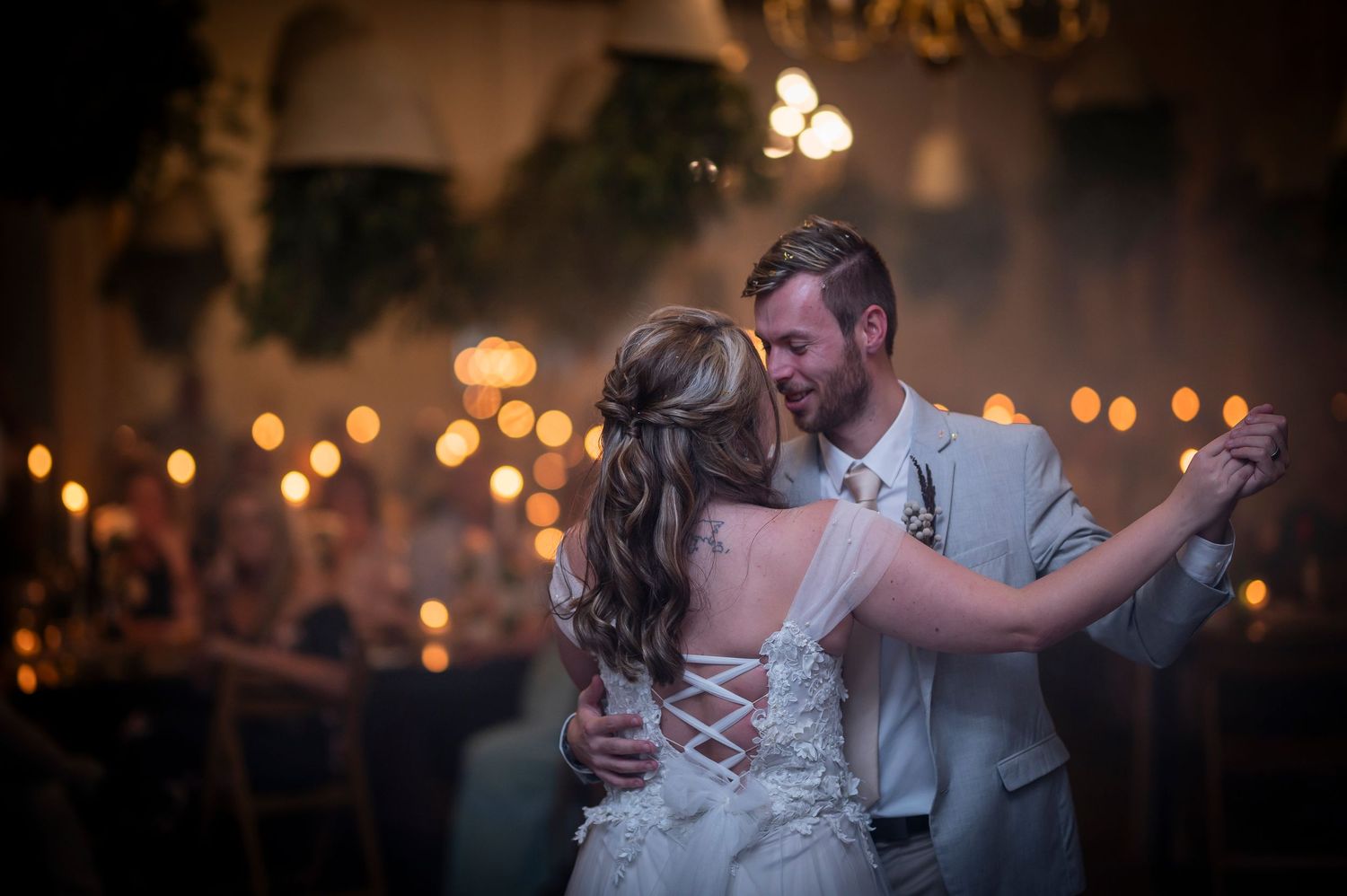 A romantic couple shares their first dance at a dimly lit wedding reception with soft bokeh lights in the background.