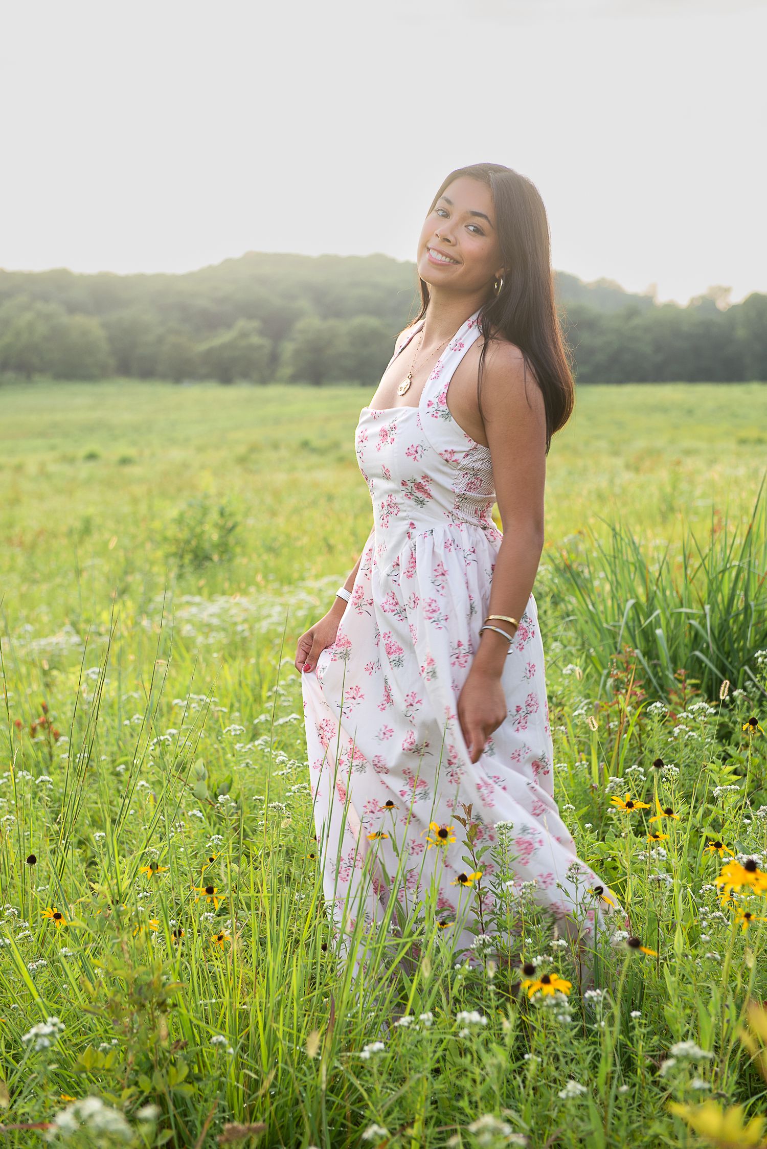 A woman in a floral white dress poses gracefully in a vibrant wildflower meadow during golden hour.