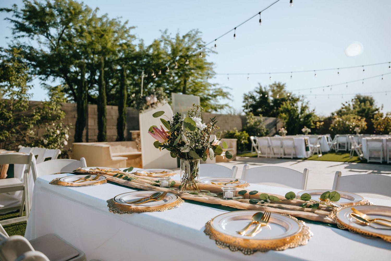 Wedding reception table settings with rustic decor and greenery outdoors.