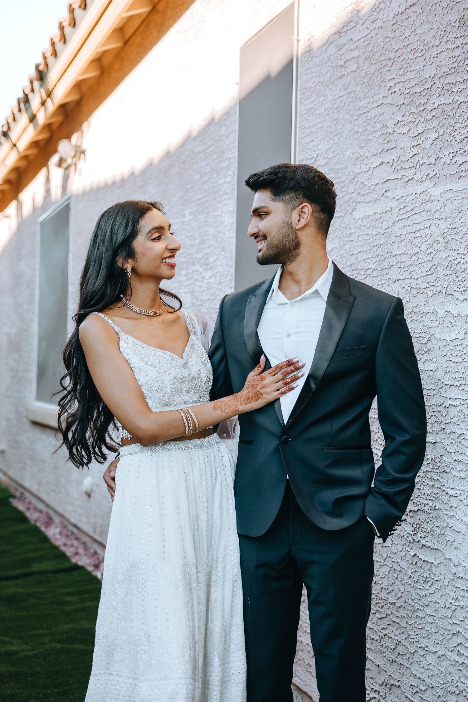 Couple in wedding attire share playful moment against white wall.