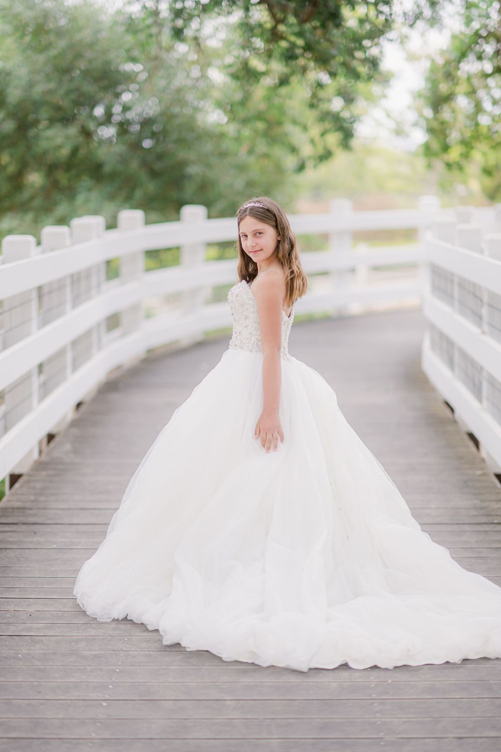 A bride in a flowing white wedding gown twirls gracefully on a wooden bridge surrounded by lush greenery.