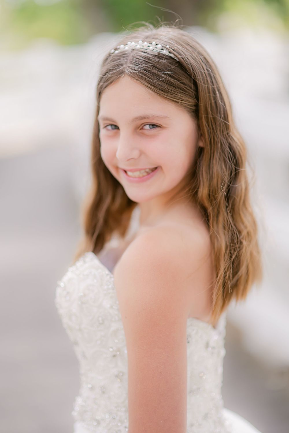 Young person smiles warmly while wearing an elegant white lace dress with a sweetheart neckline in bright natural light.
