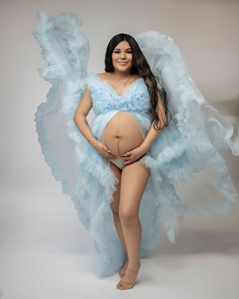 Ethereal maternity portrait series featuring flowing light blue fabric against a neutral studio backdrop.