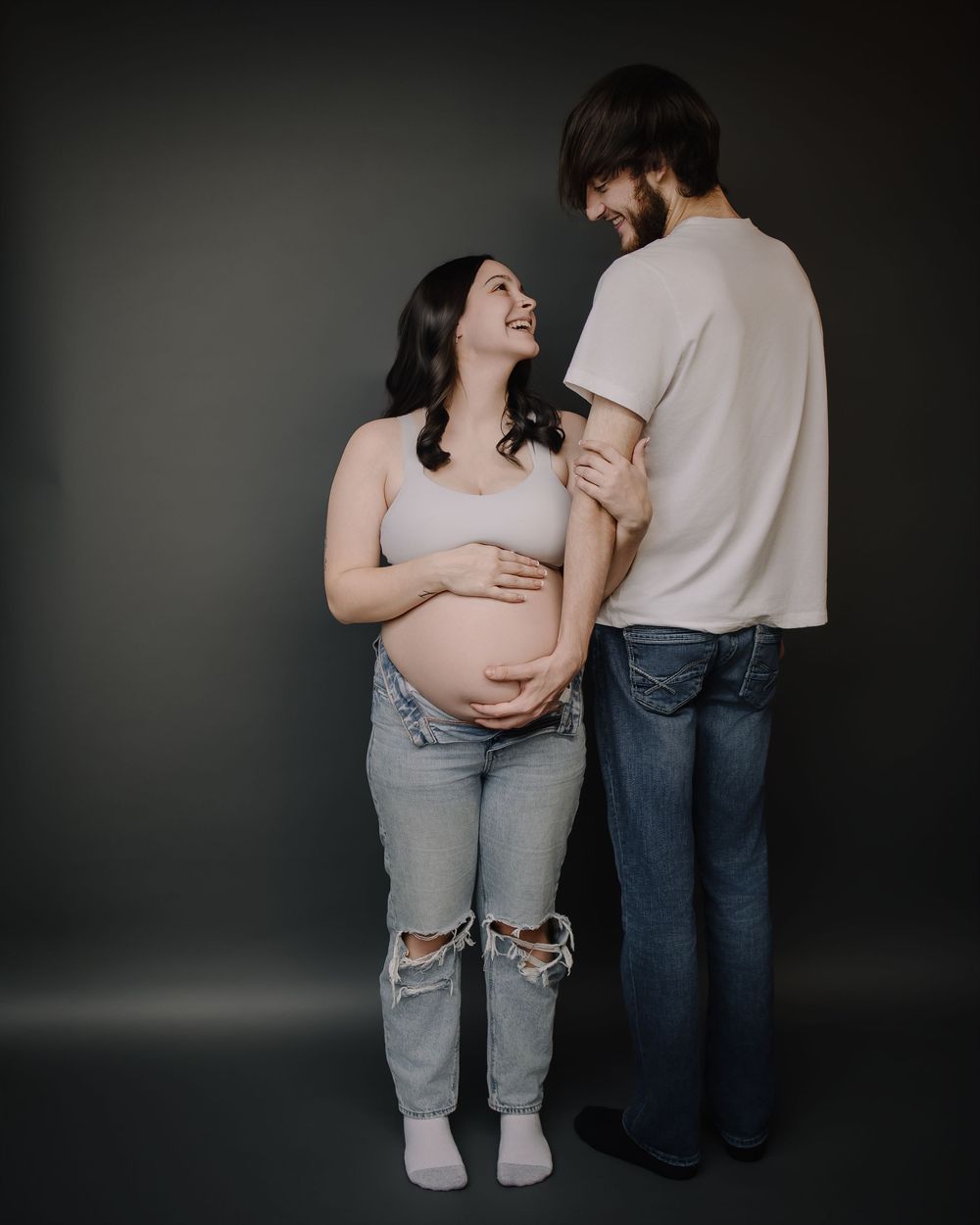 A couple shares an intimate moment together in a dark studio setting wearing casual clothing and embracing.