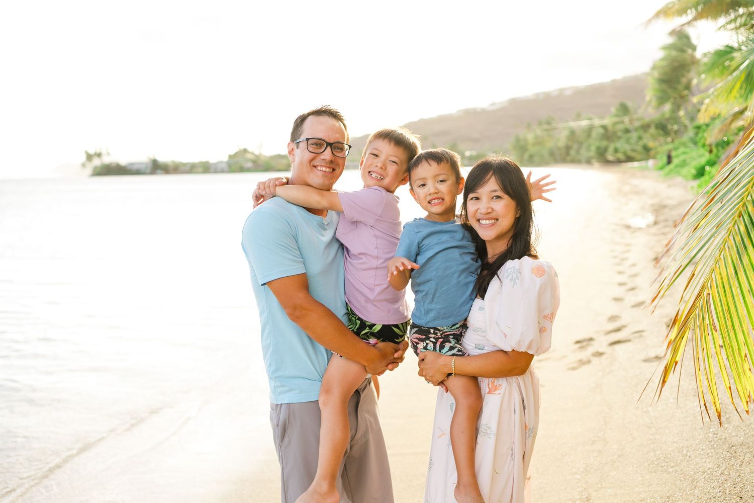 A loving family shares joyful moments together on a sunny tropical beach with palm trees and ocean views. Oahu family photographer