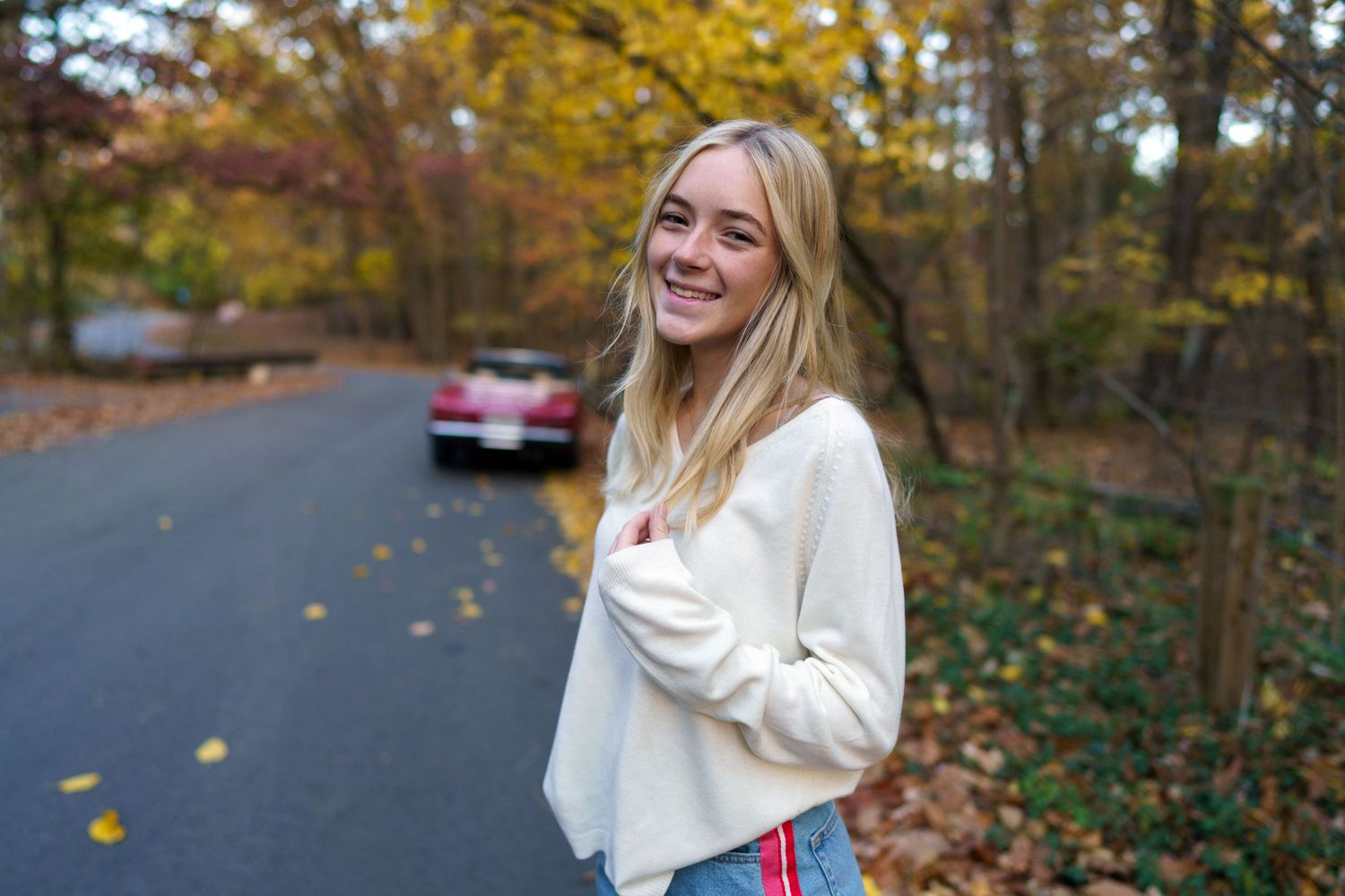 High school senior smiling on a quiet road surrounded by autumn trees, by Jamie Macey Photography in Columbus, Ohio.
