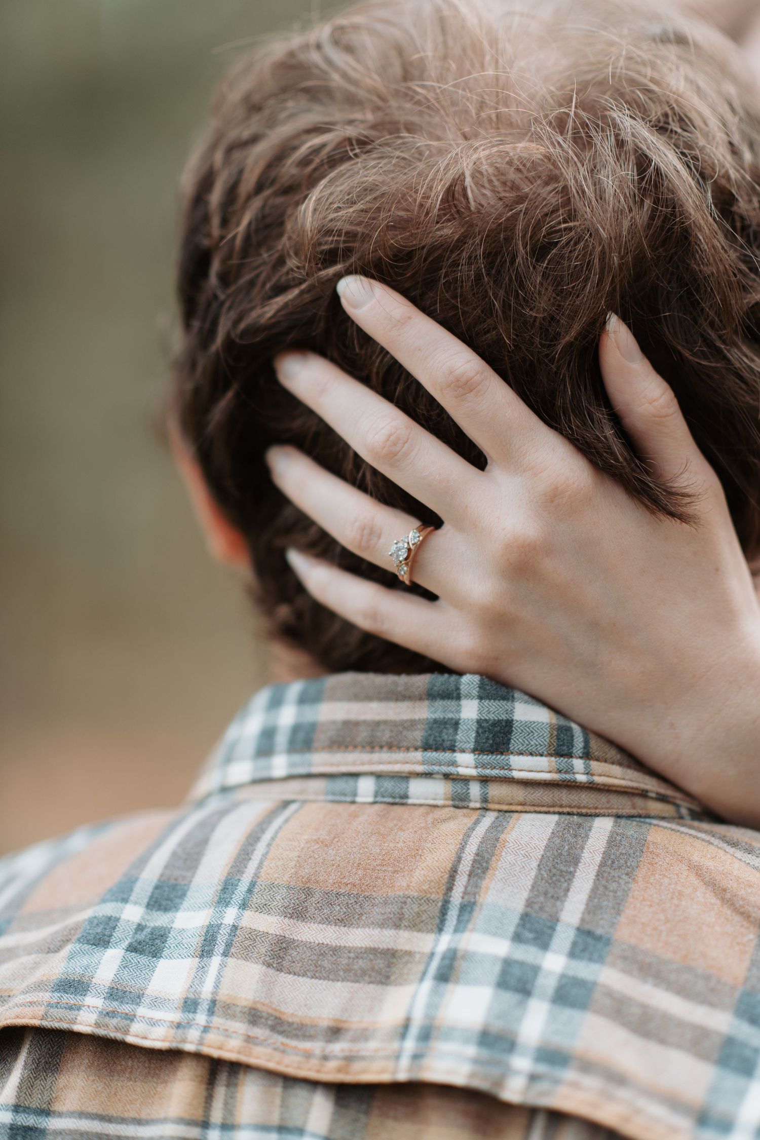 A young woman with her hand in her fiances hair with her ring sparkling in the sun during their engagement session in Post Falls, Idaho.
