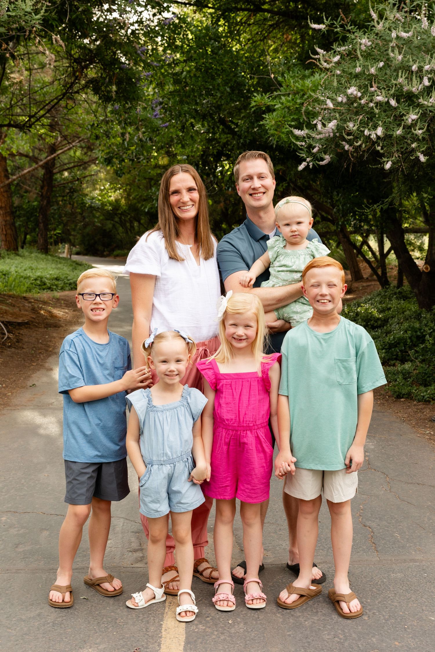a family with 5 kids smiling at the camera on a path with summer green trees behind them