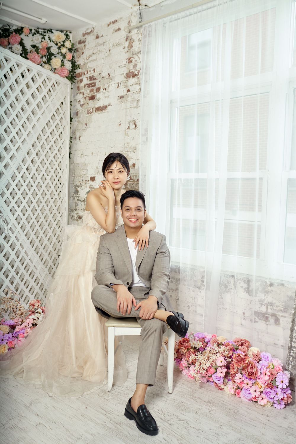 A person in a gray suit sits in a bright studio setting with floral decorations and lattice backdrop. studio photo session