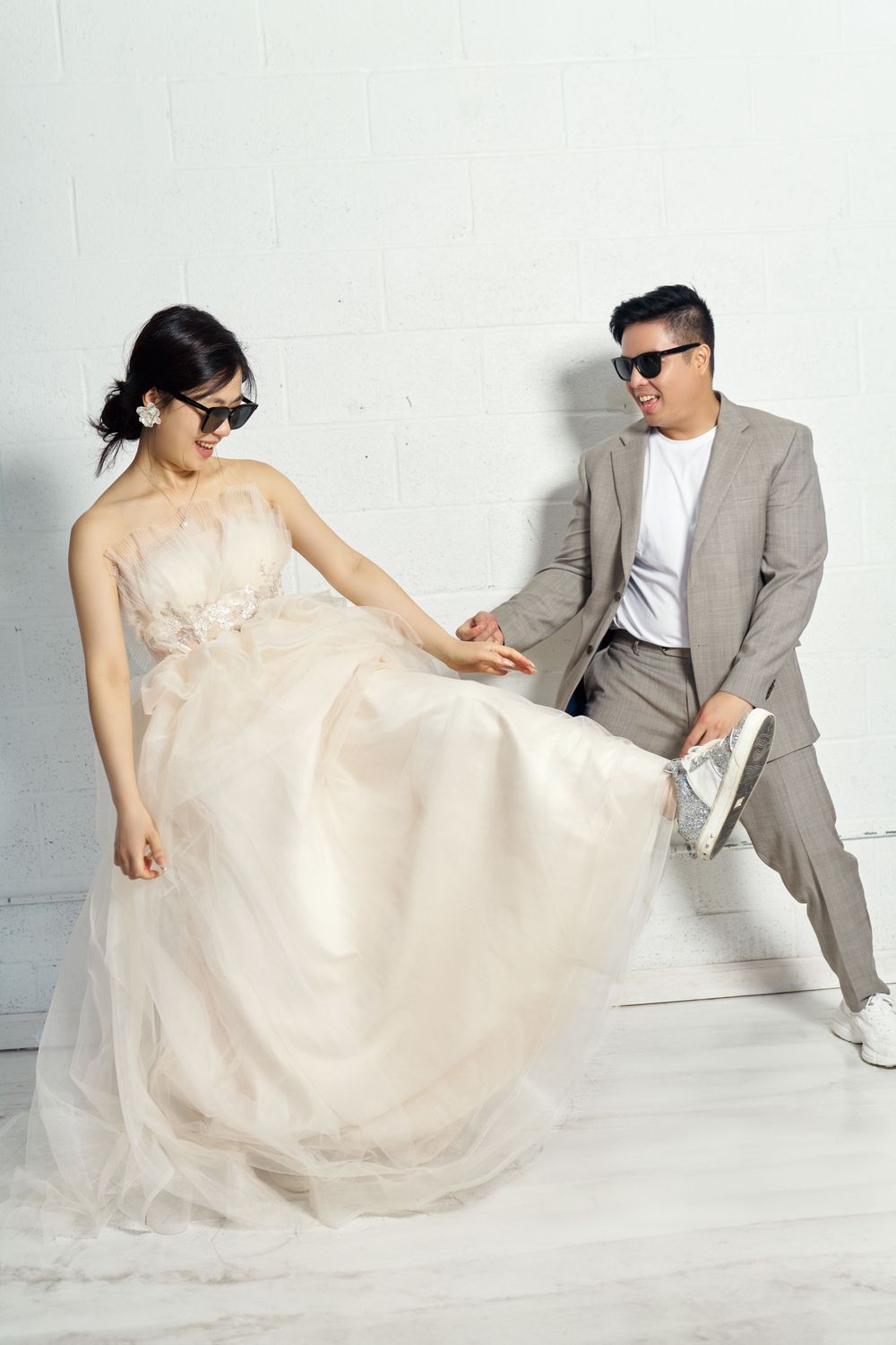 A couple in wedding attire playfully poses together on a white backdrop in a series of romantic photos. studio photo session