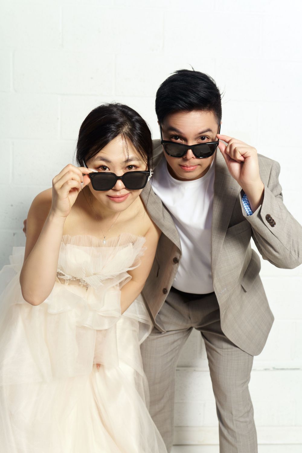 Wedding party strikes playful poses wearing sunglasses in a stylish cream and gray photoshoot series. studio photo session
