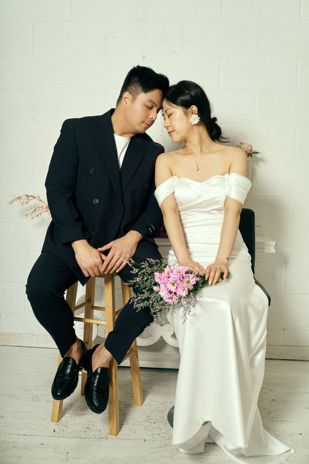 An intimate wedding moment captured as a couple share a tender pose while seated together on a wooden stool. studio photo session