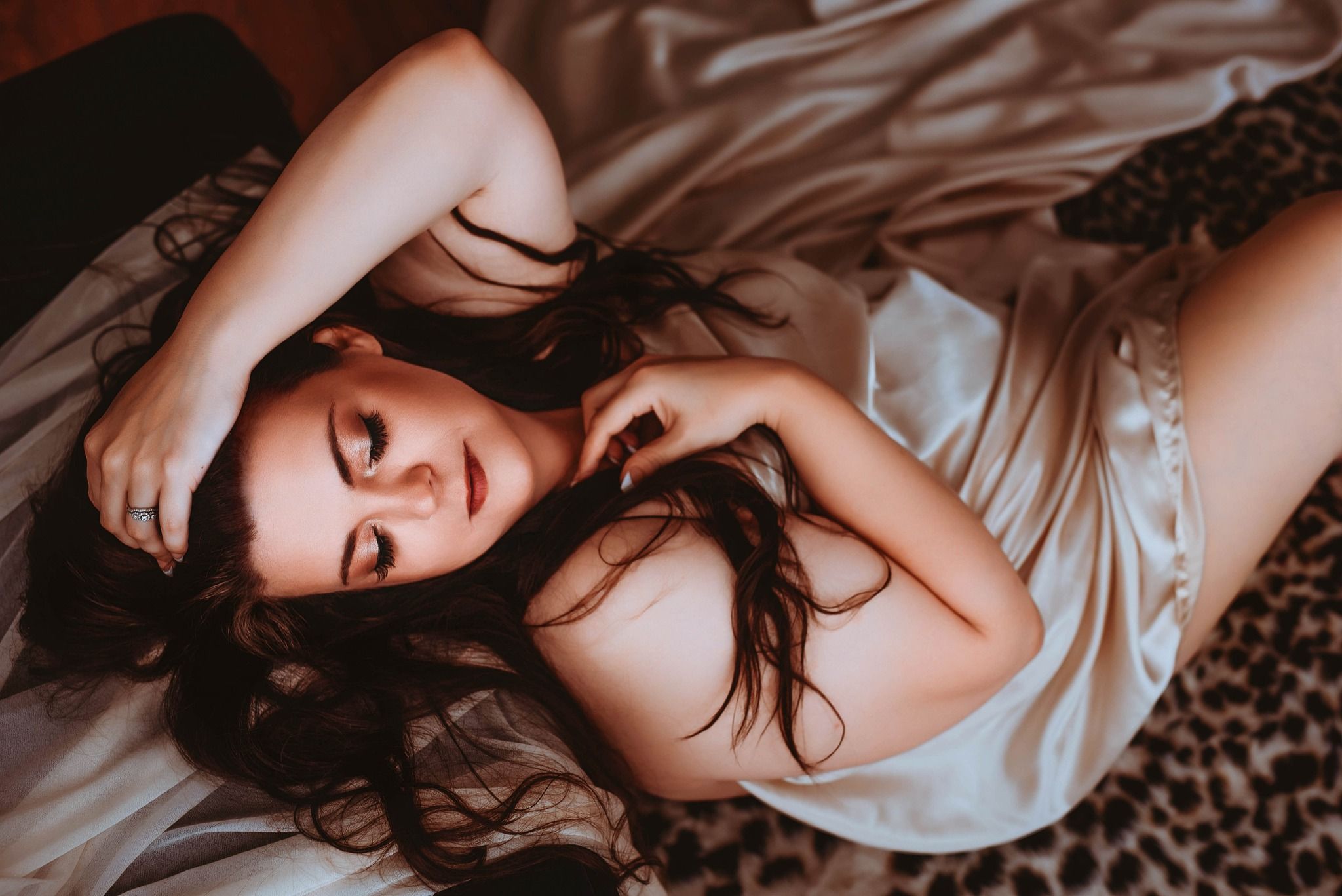 Intimate lifestyle photography series showing soft poses on white bedding with moody lighting.