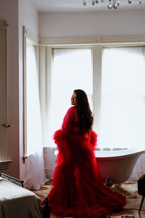 A series of dramatic photographs showing a figure in a flowing red tulle gown posing near bright windows in an elegant room.