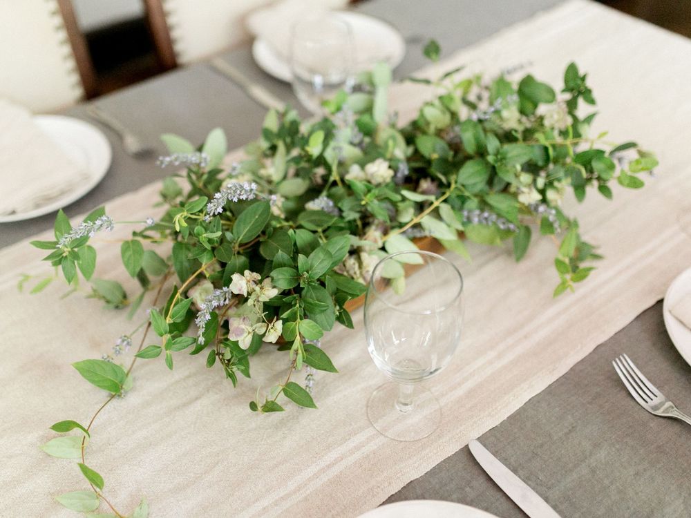 Fresh greenery and floral arrangements displayed along a light wooden table setting.