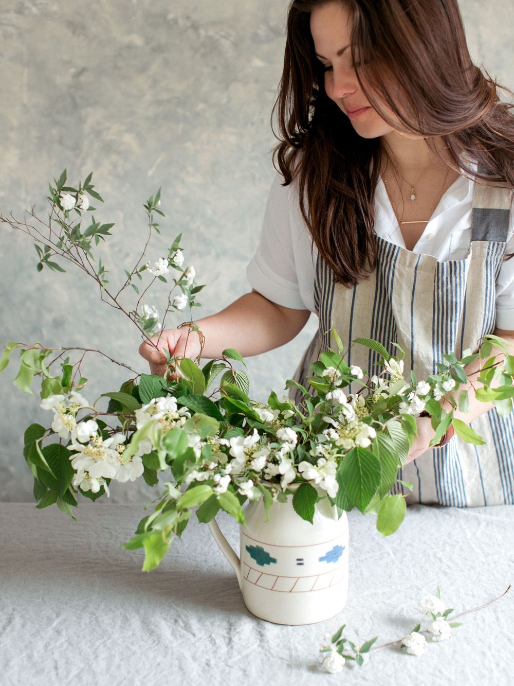 Someone arranging delicate white flowers and greenery in a blue and white striped ceramic vase for a floral display.