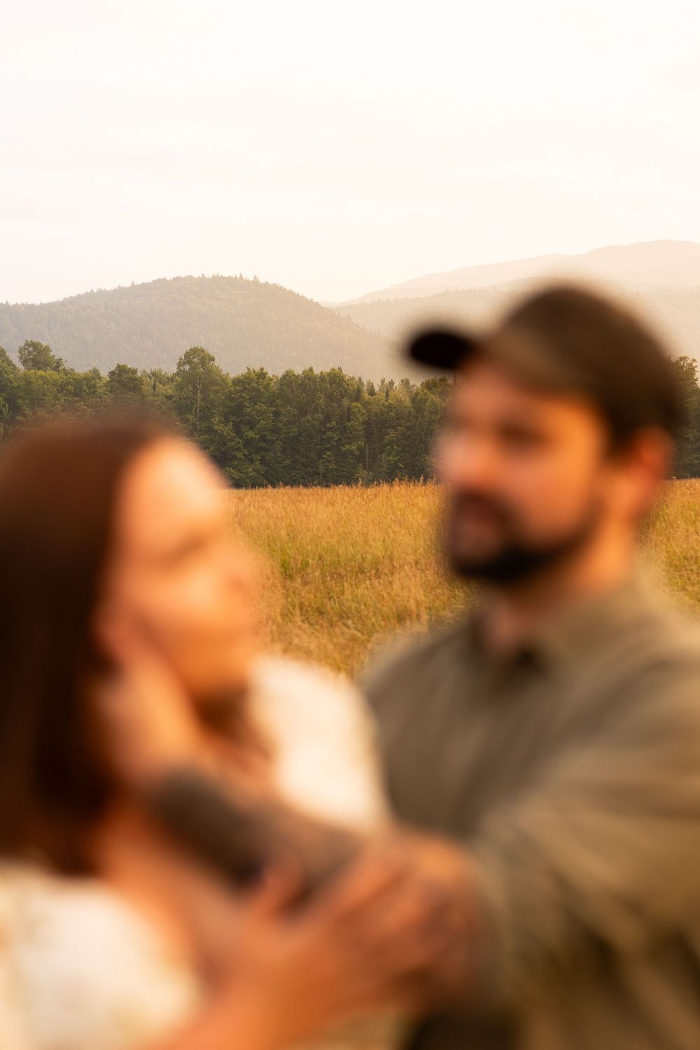 Couple sharing an intimate moment in a golden field with mountains in the distance during sunset.