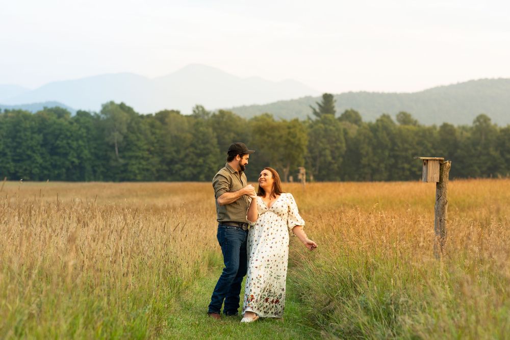 Romantic couple embracing in a golden wheat field at sunset with mountains in the background.