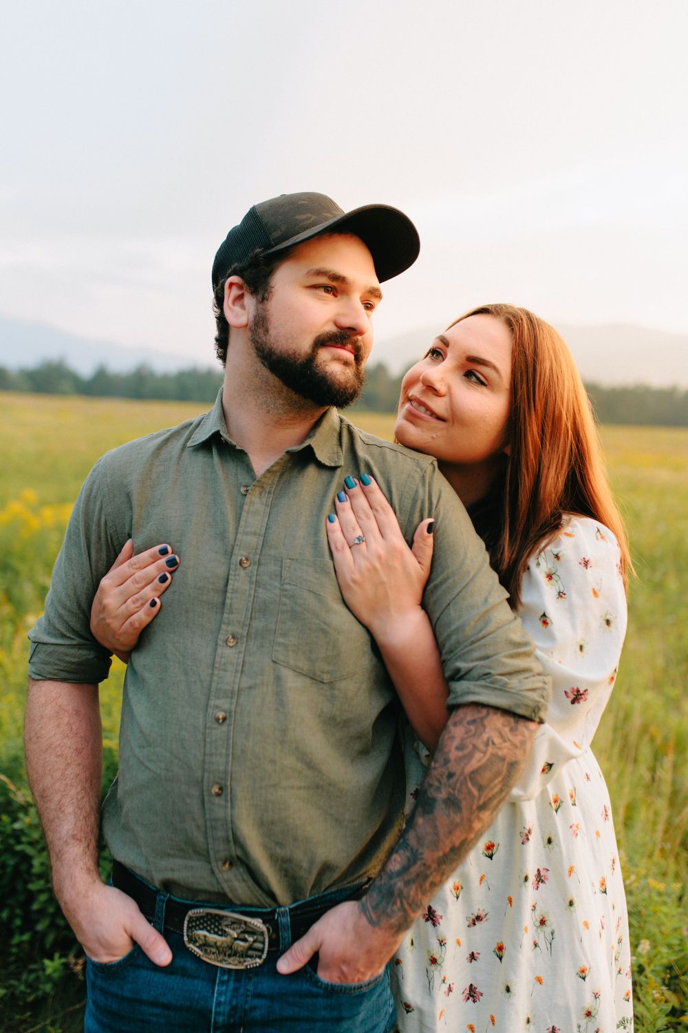 A tender embrace between a couple in casual clothing standing in a wildflower field at golden hour.
