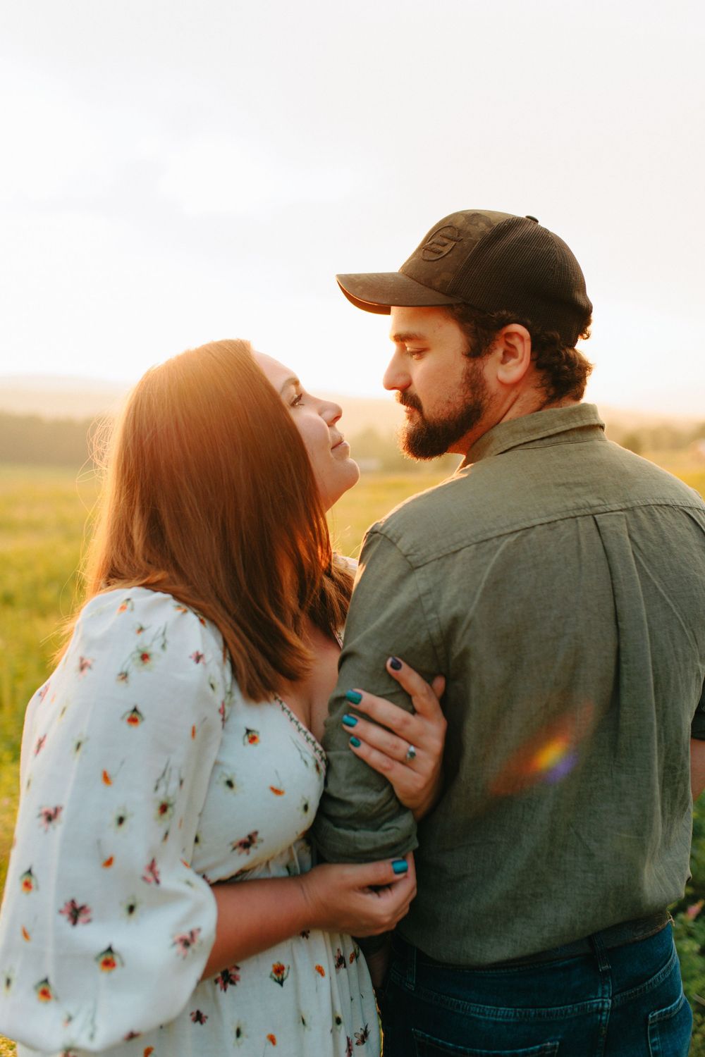 A couple embraces in a sunlit field wearing casual clothing during golden hour.