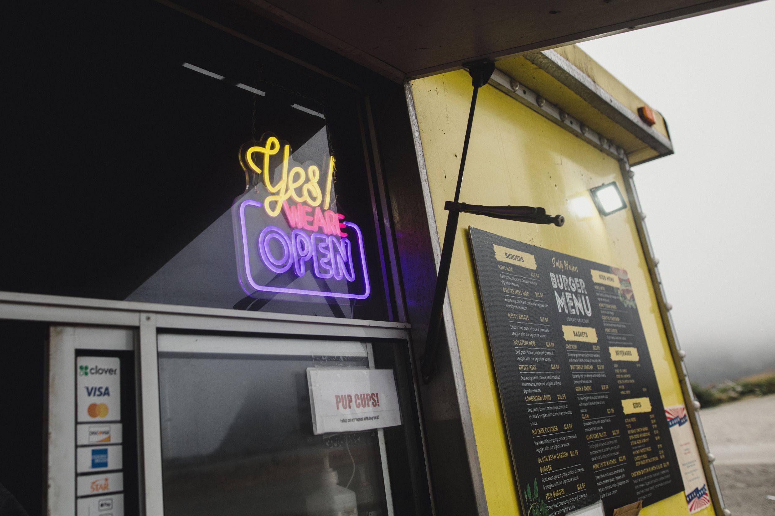 Food truck with illuminated neon signs and menu boards displayed outside.