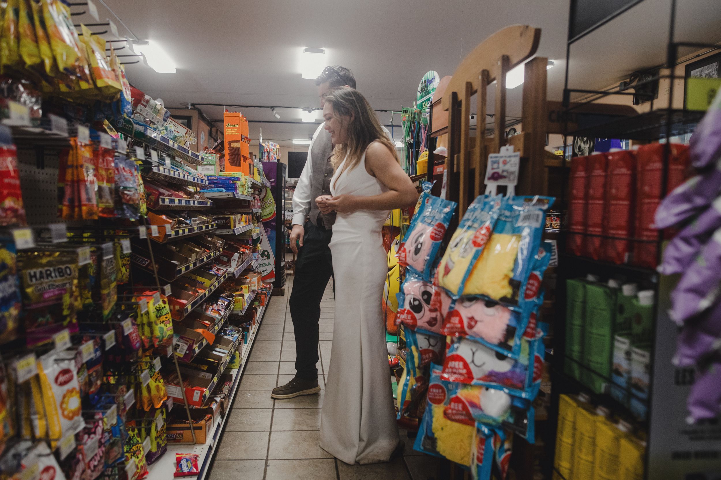 Bride shopping in convenience store aisle while wearing wedding dress.