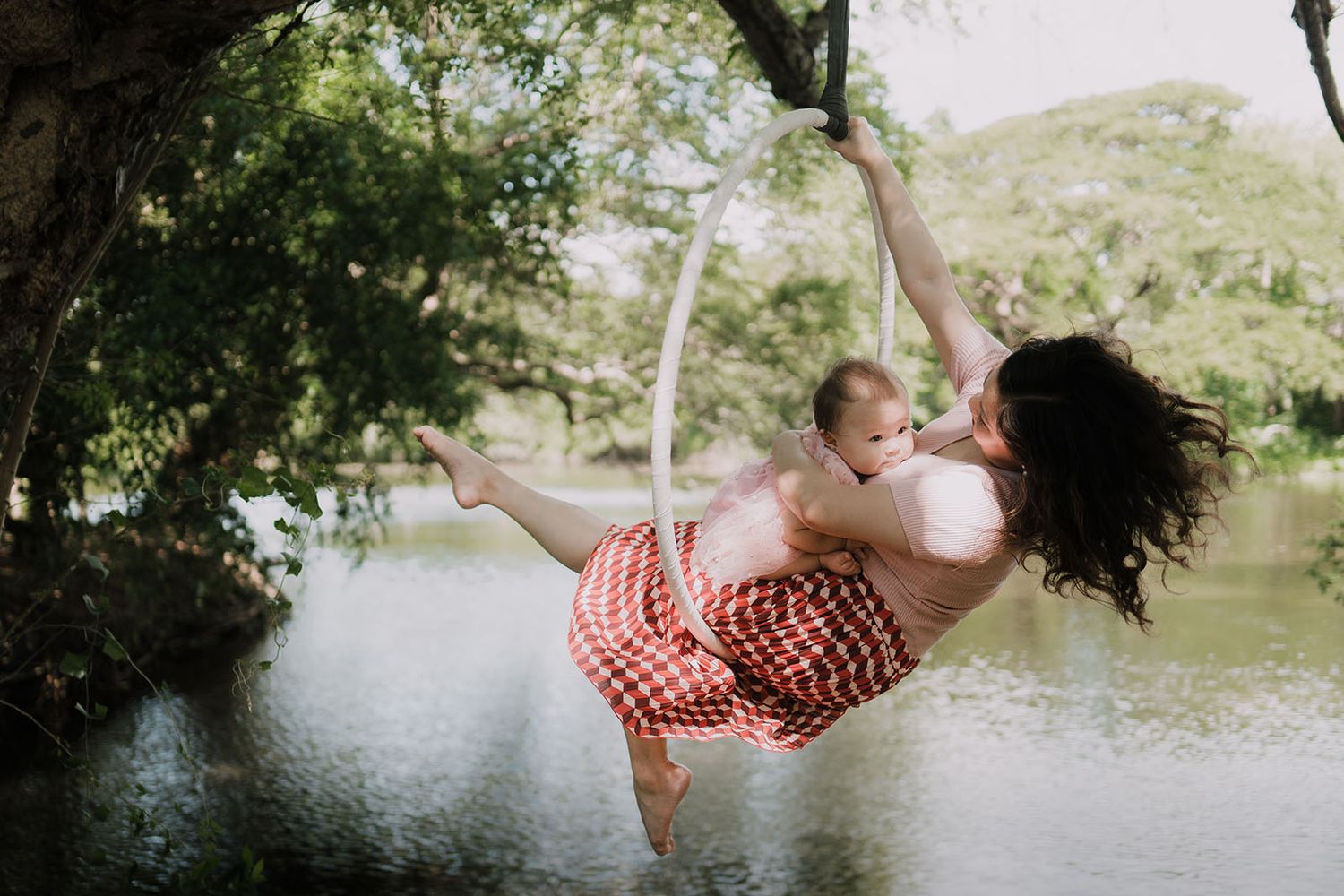 People swinging on ropes over a tranquil lake surrounded by trees.