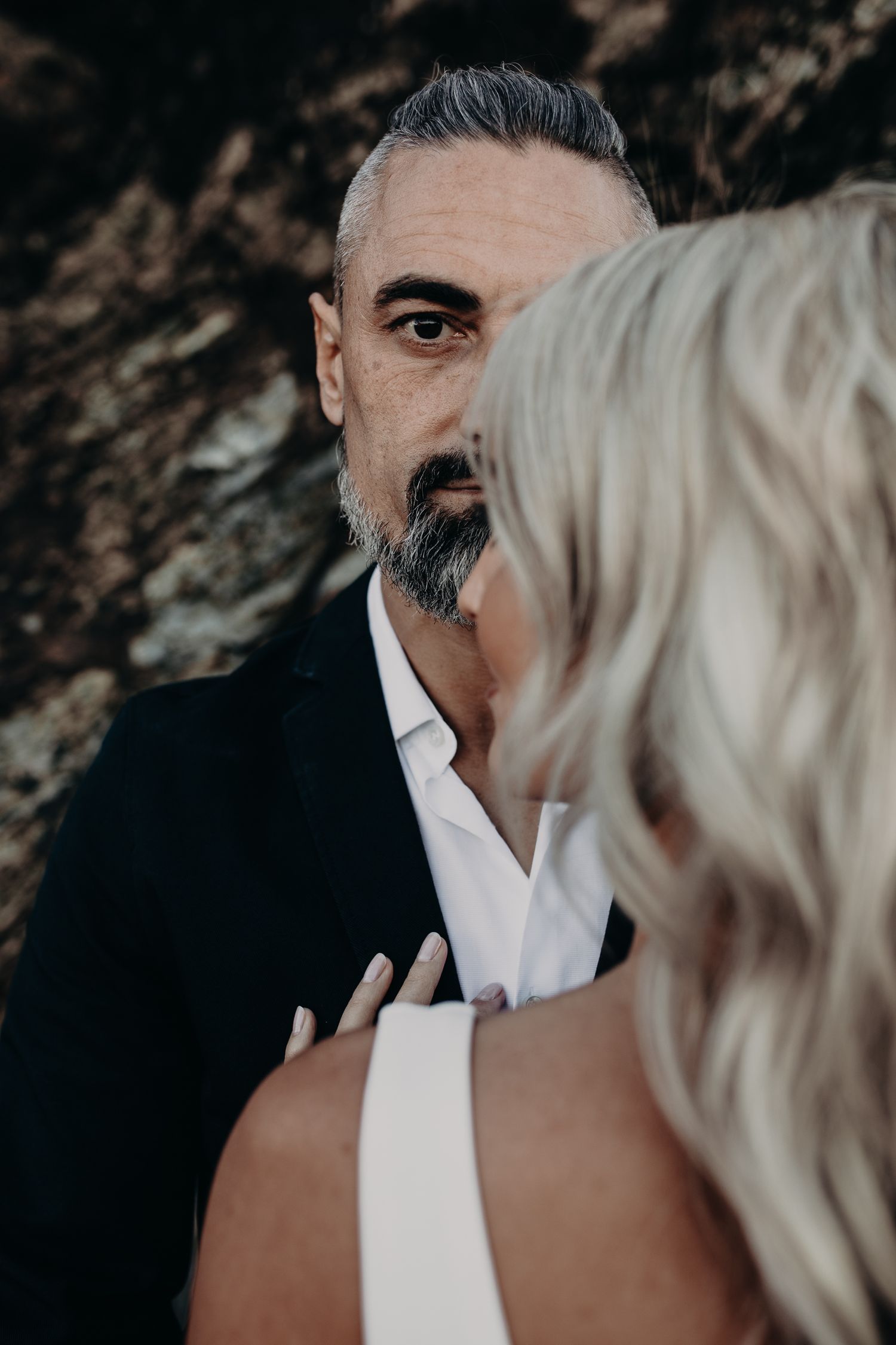 Close-up portrait of a couple in wedding attire posing intimately against a rocky background.