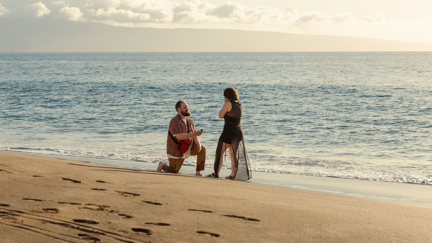 Two people share an intimate moment during a beach proposal at sunset with ocean waves in the background.