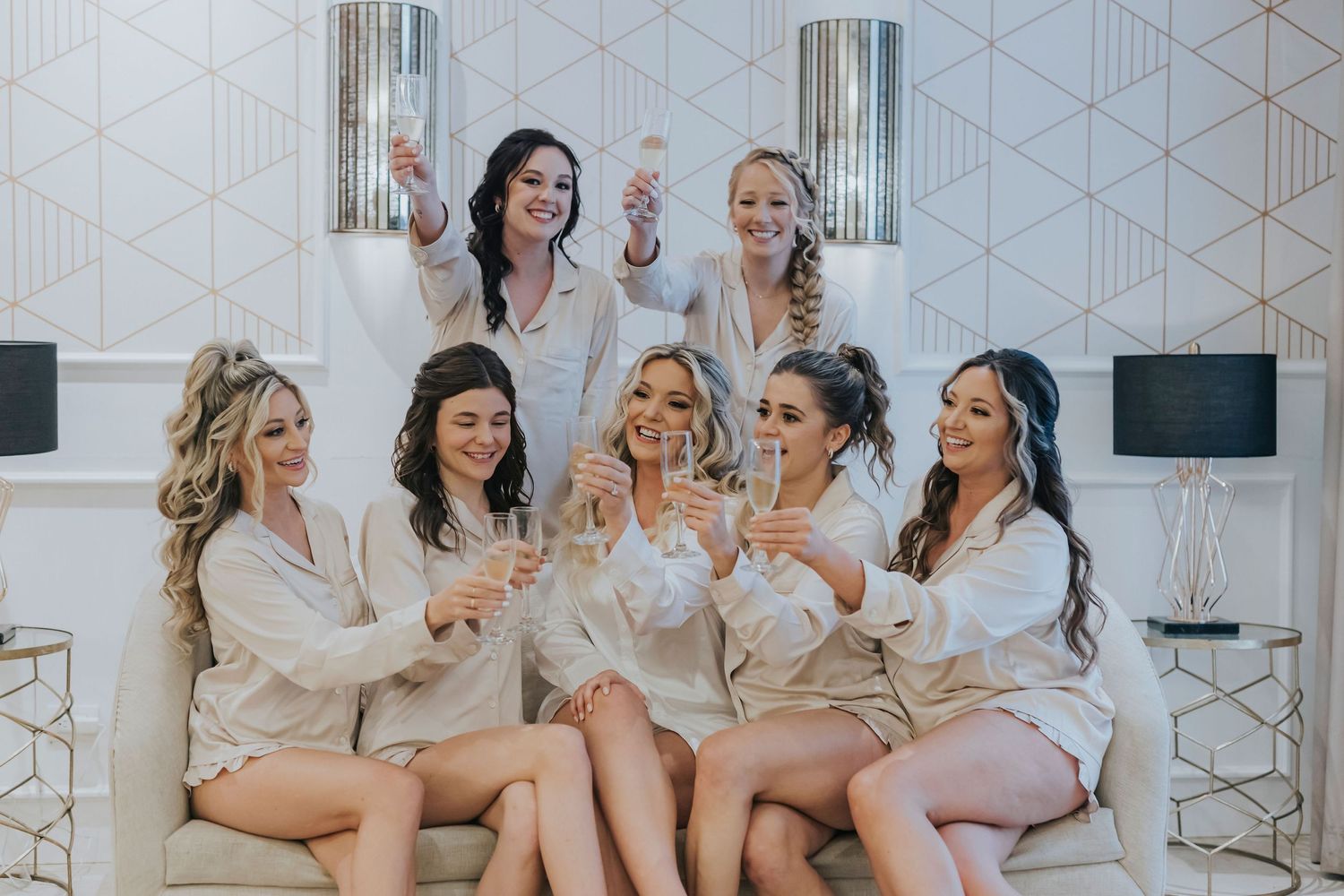Group in white robes celebrating with champagne during pre-wedding preparations.