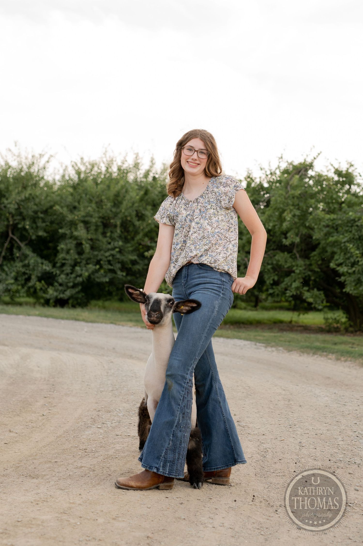 A portrait on a country path featuring bell-bottom jeans, a floral top, and a show lamb companion.