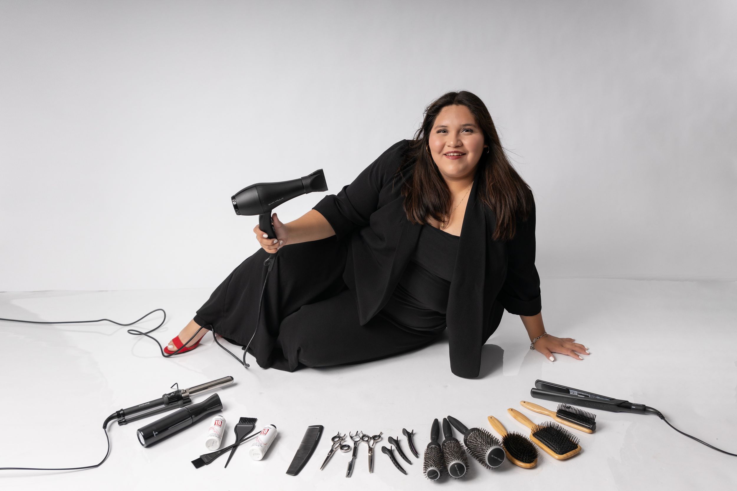 Professional hairstyling tools and accessories including curling irons, brushes and dryers arranged on white surface.