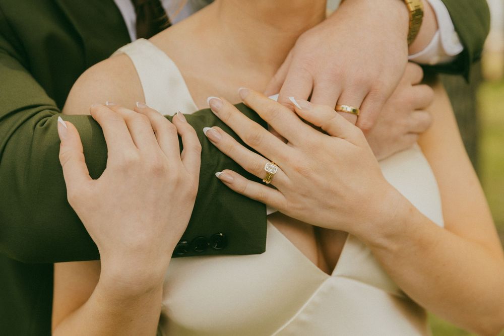 Close-up of wedding couple hands showing engagement and wedding rings, bride in white dress, groom in dark suit.
