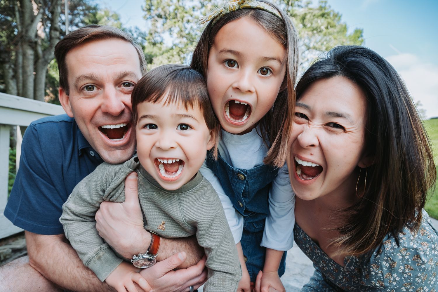 A family shares a joyful moment together while standing on a wooden bridge surrounded by green trees.
