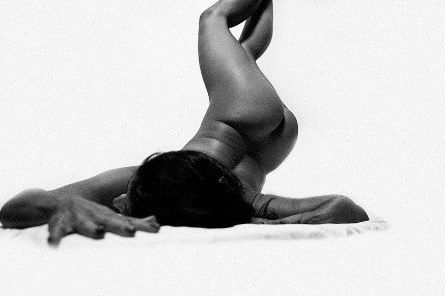 A black and white artistic photo of a dancer lying on the floor in a curved, graceful pose.