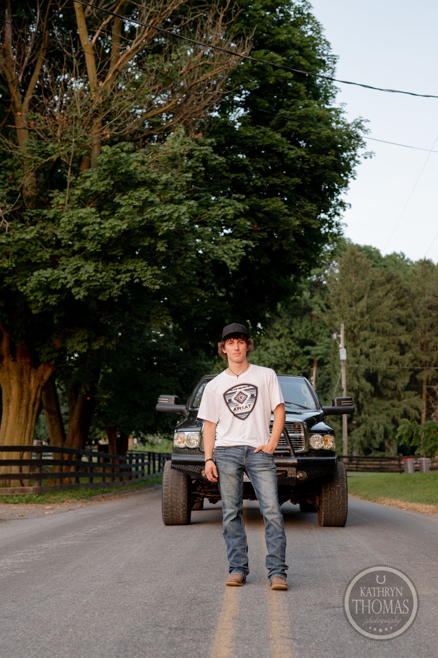 Modified black Dodge Ram truck parked on tree-lined rural road.