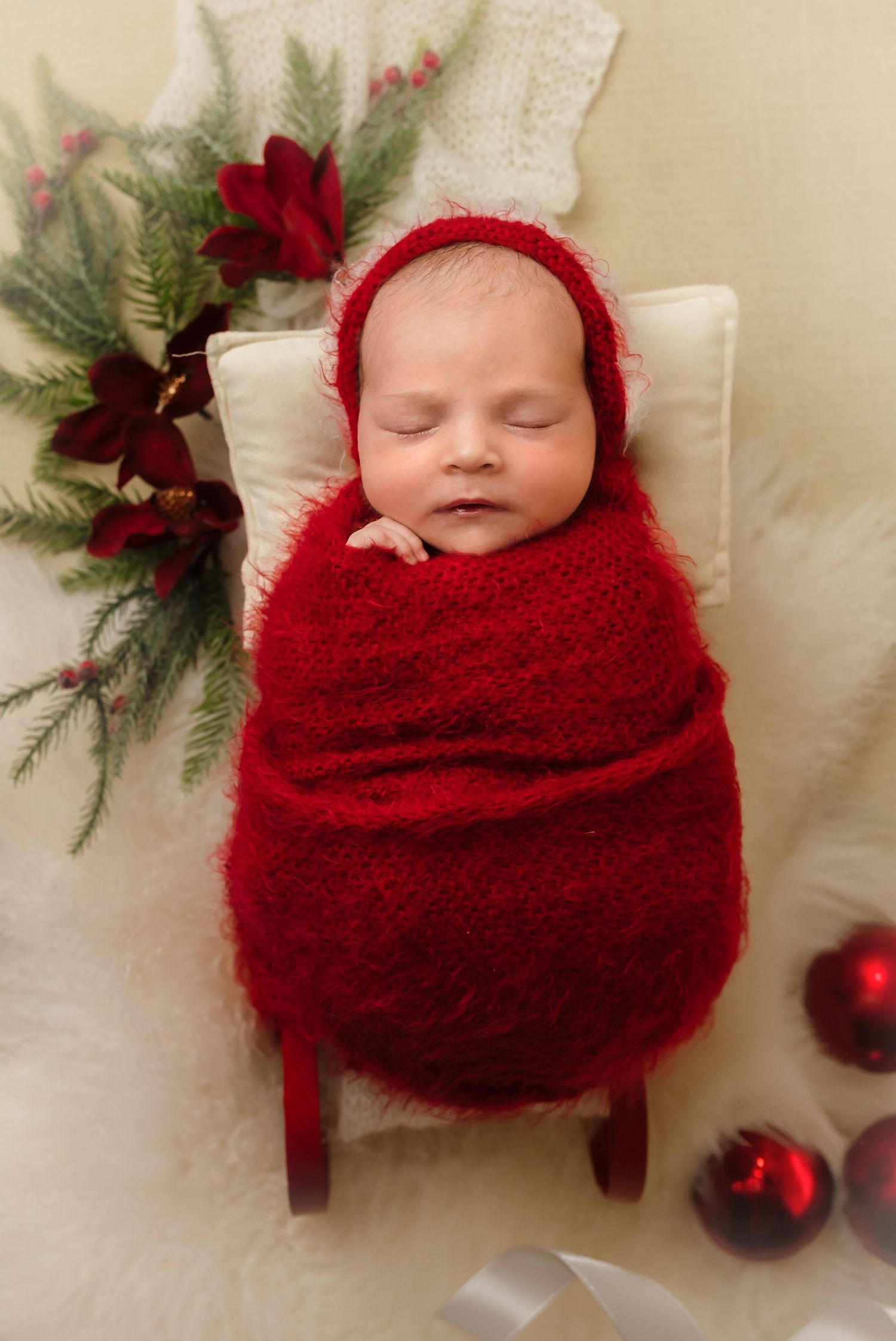 Harrisonburg photographer, newborn, baby, family, and maternity, baby in a red wrap on a miniature red sleigh and with poinsettias