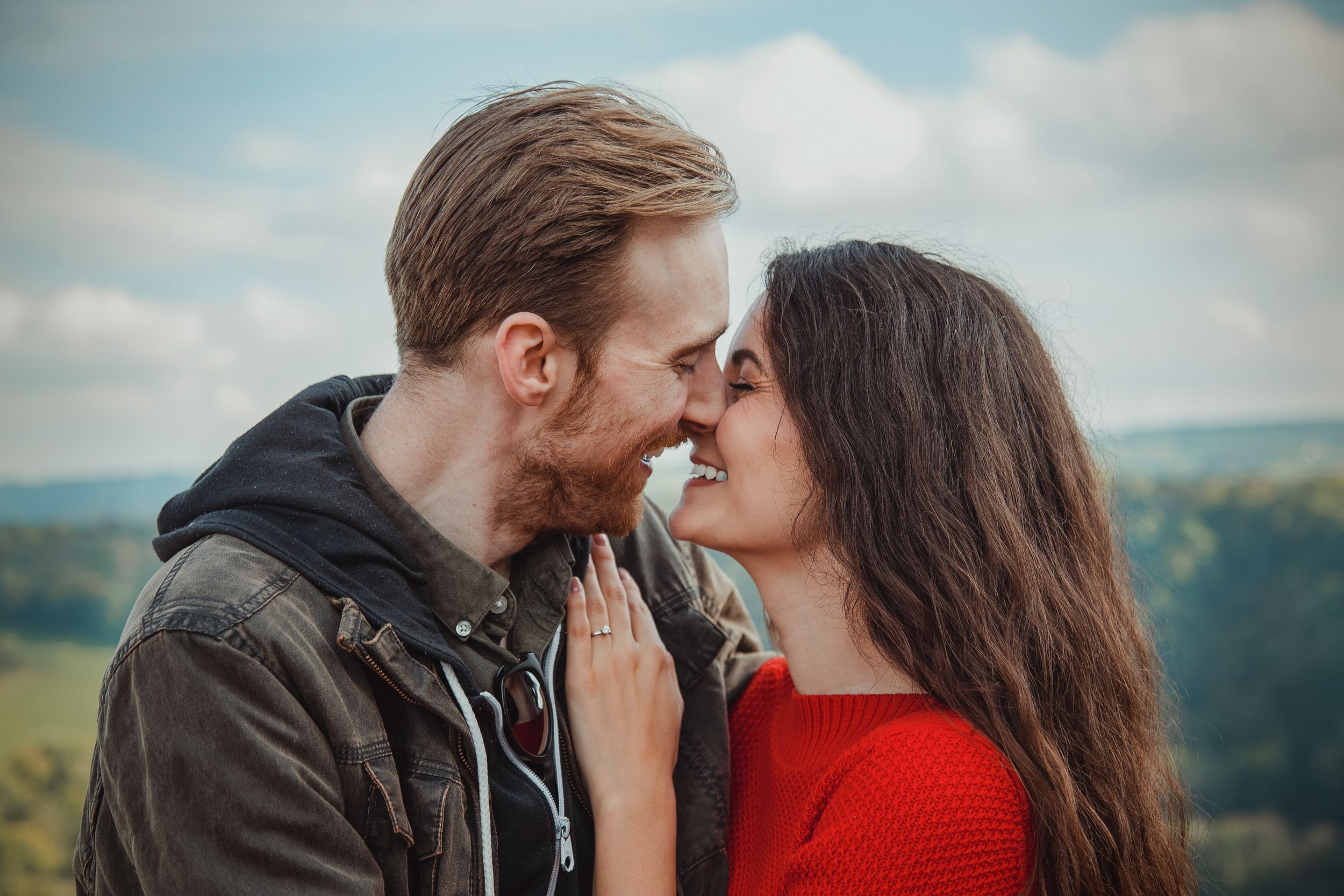 Romantic couple sharing an intimate moment against a scenic countryside backdrop.