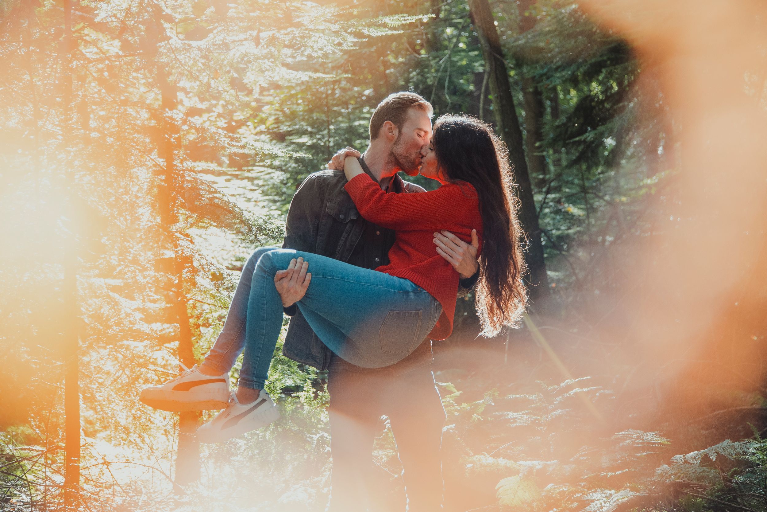 A romantic couple shares tender moments in a sunlit forest setting.
