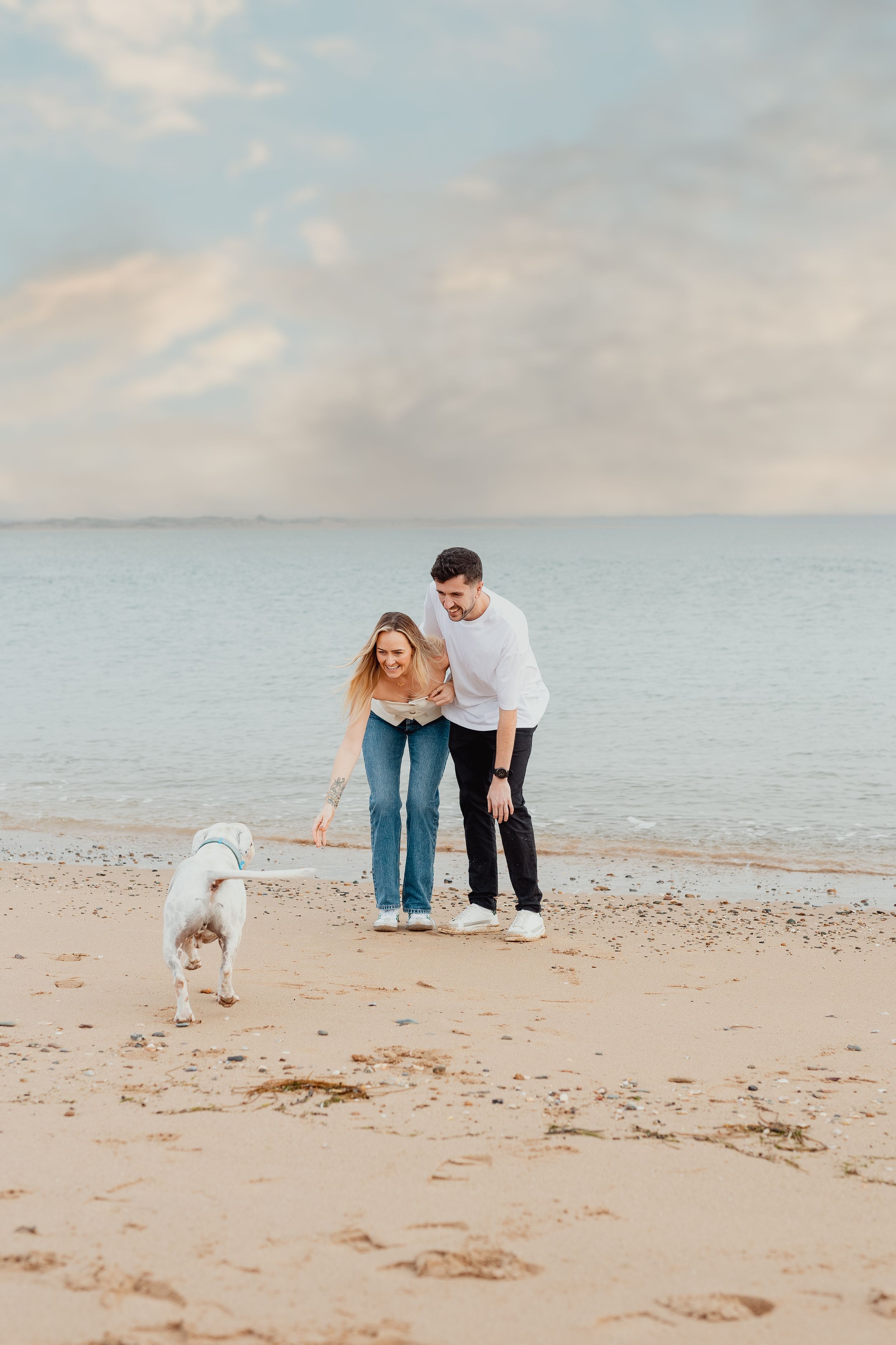 Couple walking their white dog along a peaceful beach at dusk.