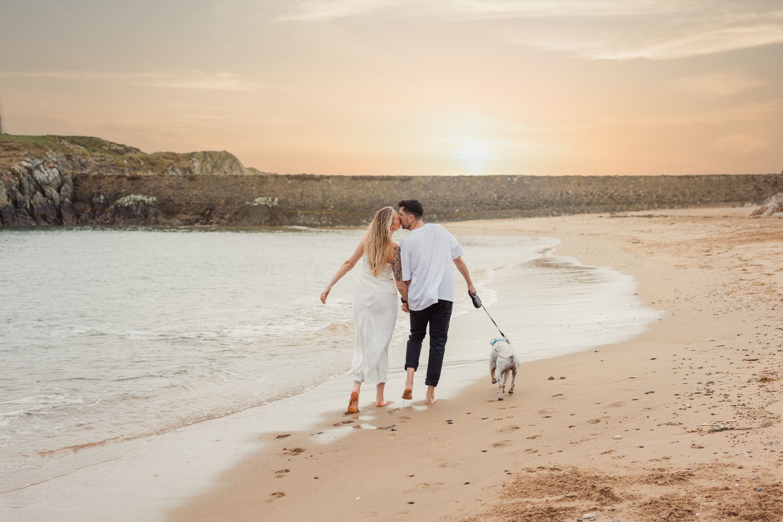 Couple and their dog enjoying a sunset walk along a scenic beach.