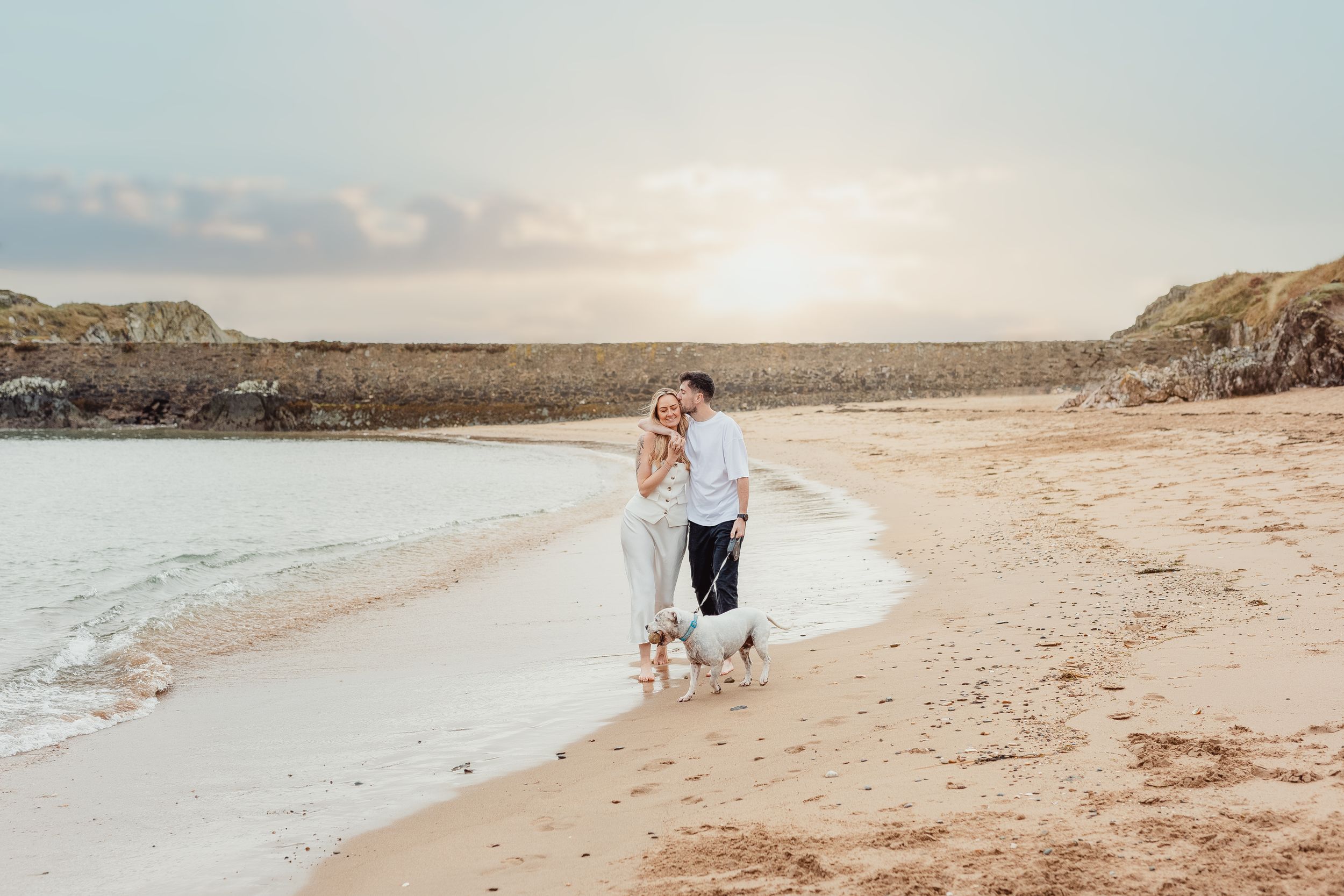 Couple walking along shoreline during golden hour at a scenic beach.