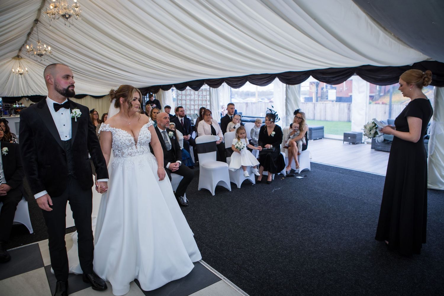 Wedding ceremony taking place in an elegant draped tent with guests seated and looking on.